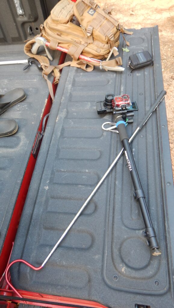Field gear on a truck tailgate: a snake hook, snake tongs, a camera on an extension pole and a field pack