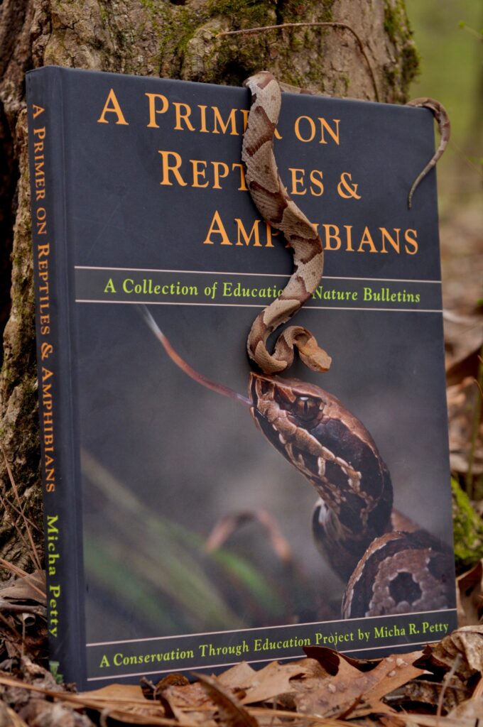 A copy of A Primer on Reptiles & Amphibians propped against a mossy tree trunk in the woods.